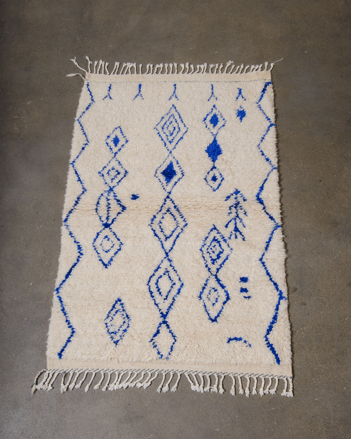 Berberlin Azilal rug in cream wool with blue cotton laying on a grey concrete floor.